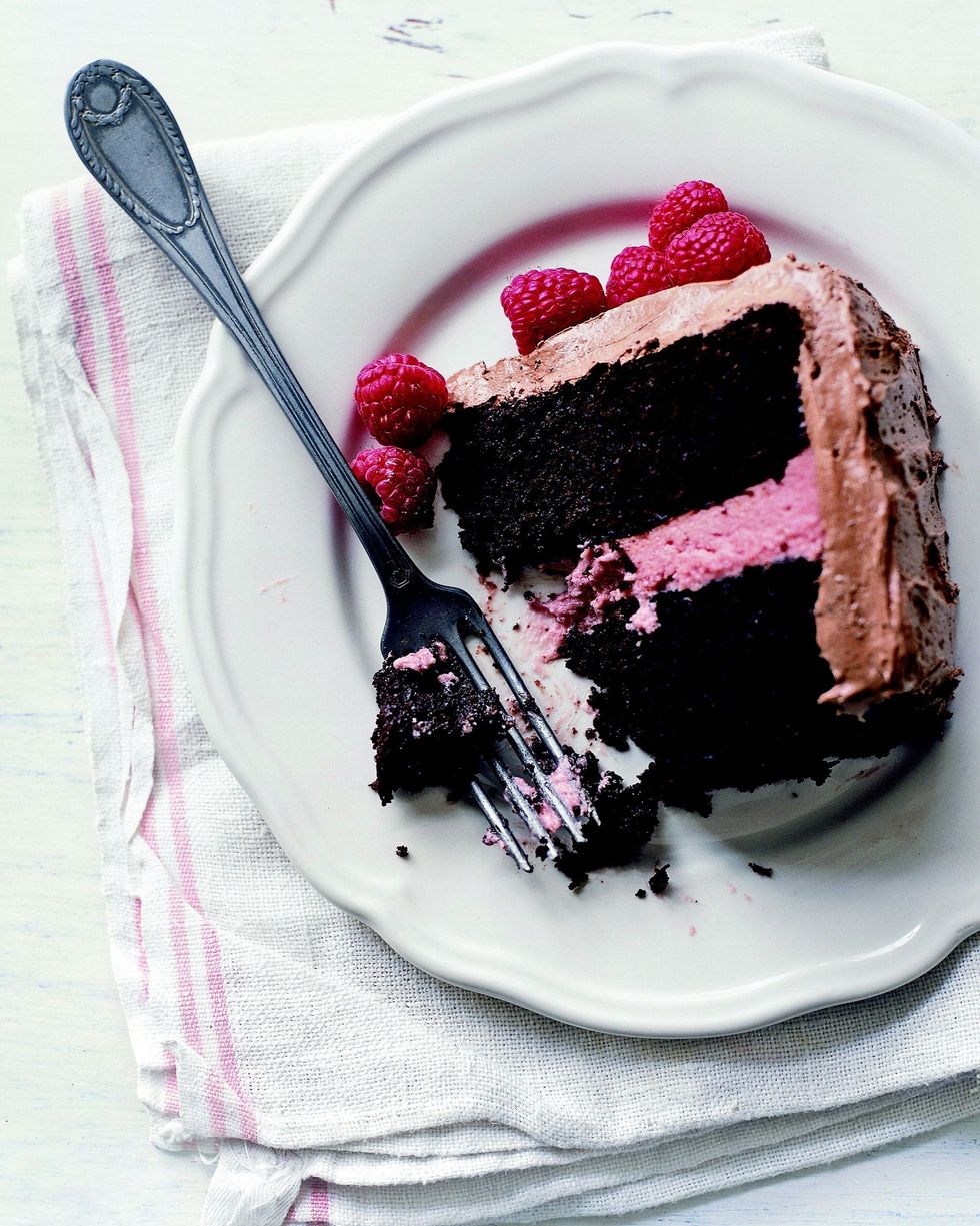 a slice of deep dark chocolate cake with raspberry filling and chocolate frosting with raspberries for garnish
