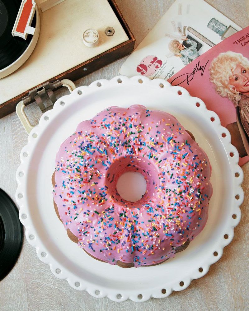 dollys donut coconut bundt cake on a white plate with pink glaze and sprinkles on top