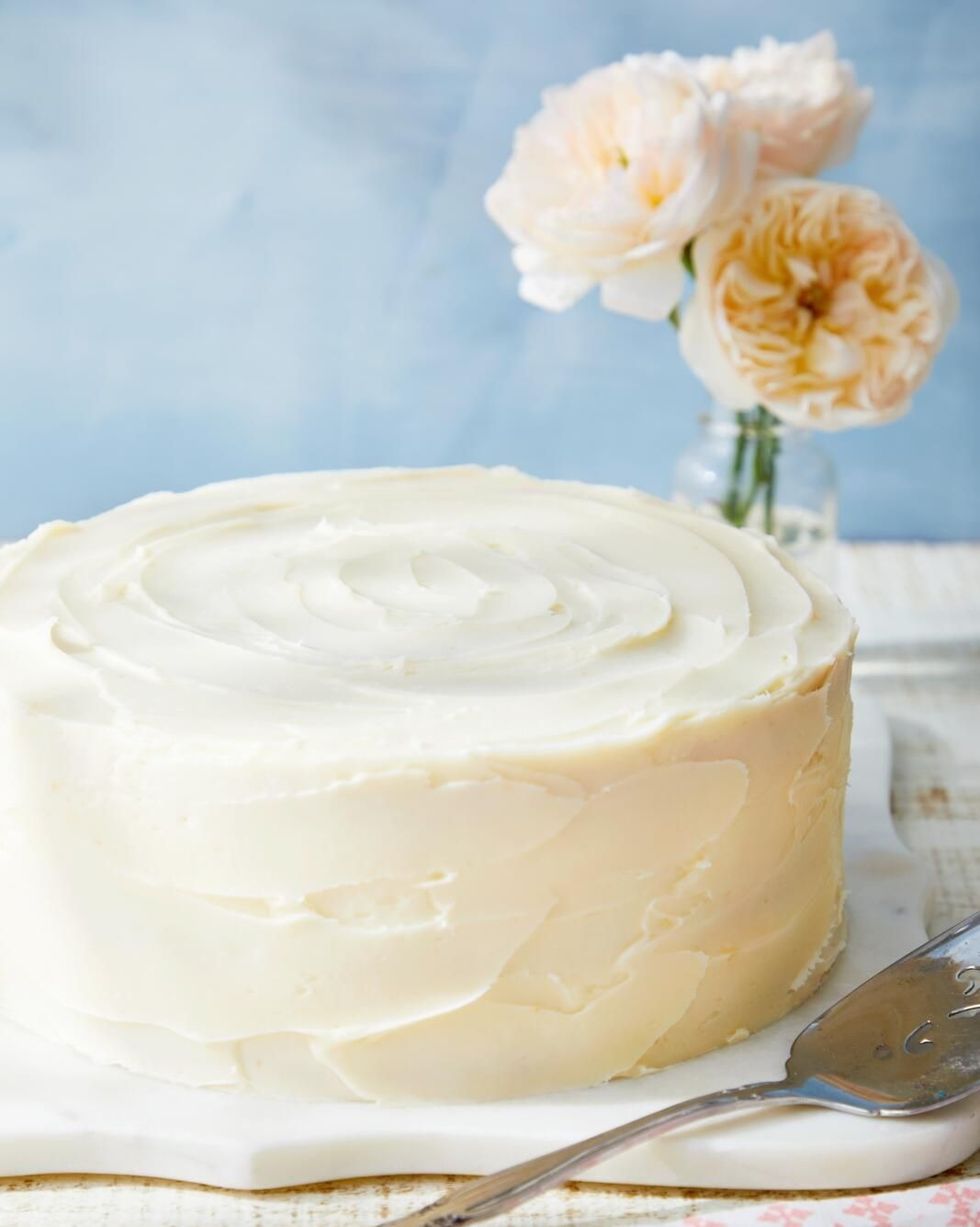 gluten free vanilla cake with vanilla frosting on a white serving board with a cake server