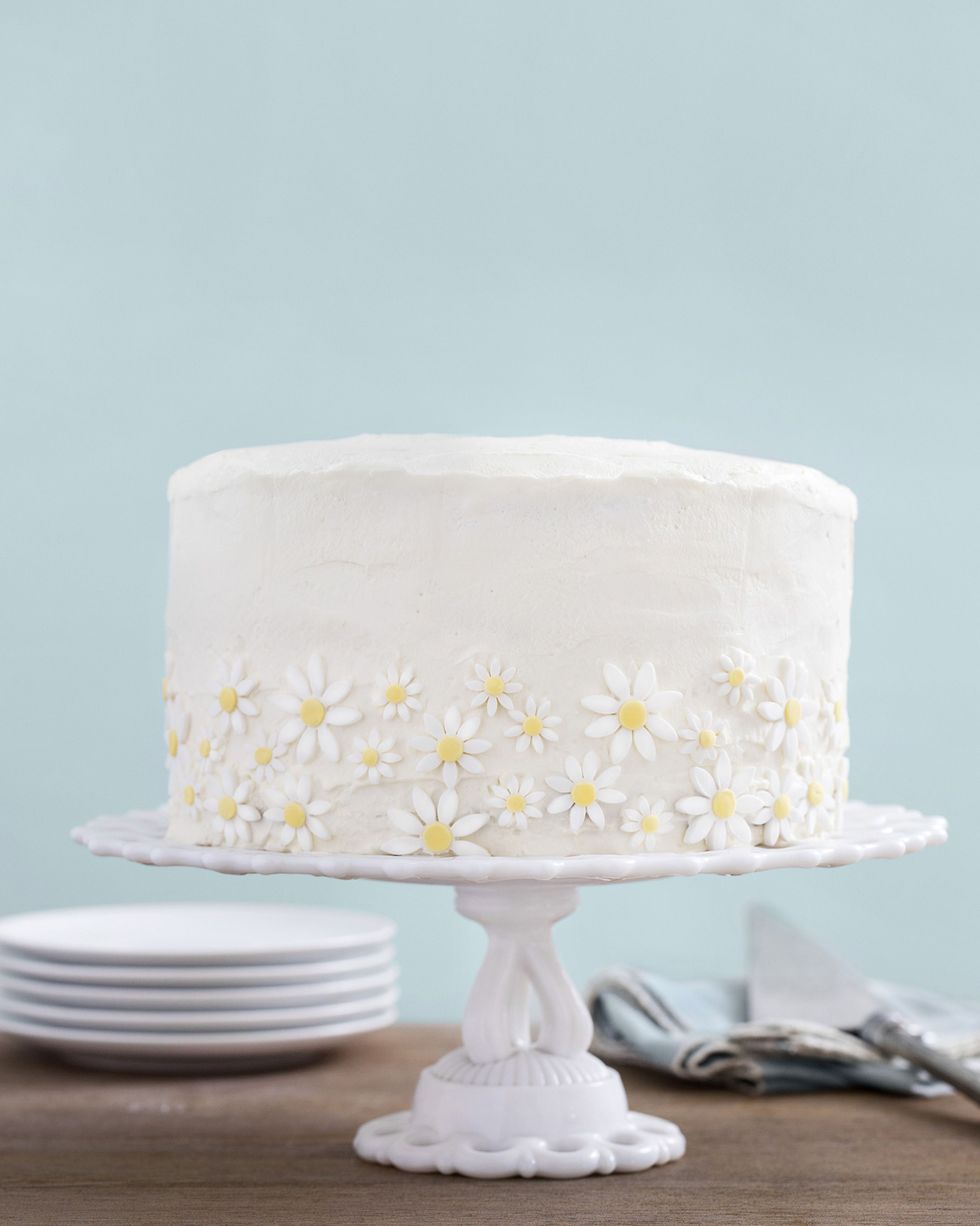 lemon coconut cake with white frosting and decorated with small sugar daisies on the sides