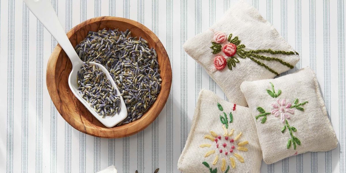 four small linen sachets embroidered with flower designs beside a bowl of dried lavender and a scoop