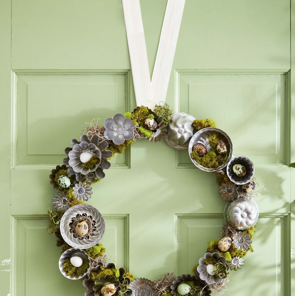 handcrafted moss wreath decorated with faux quail eggs and small tart tins to mimic nests, hung on green door