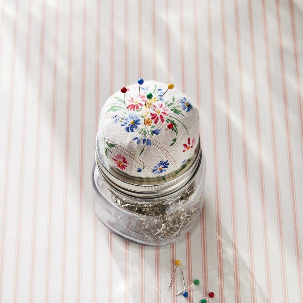 jar filled with pins, topped with a padded decorative floral lid that serves as a pin cushion