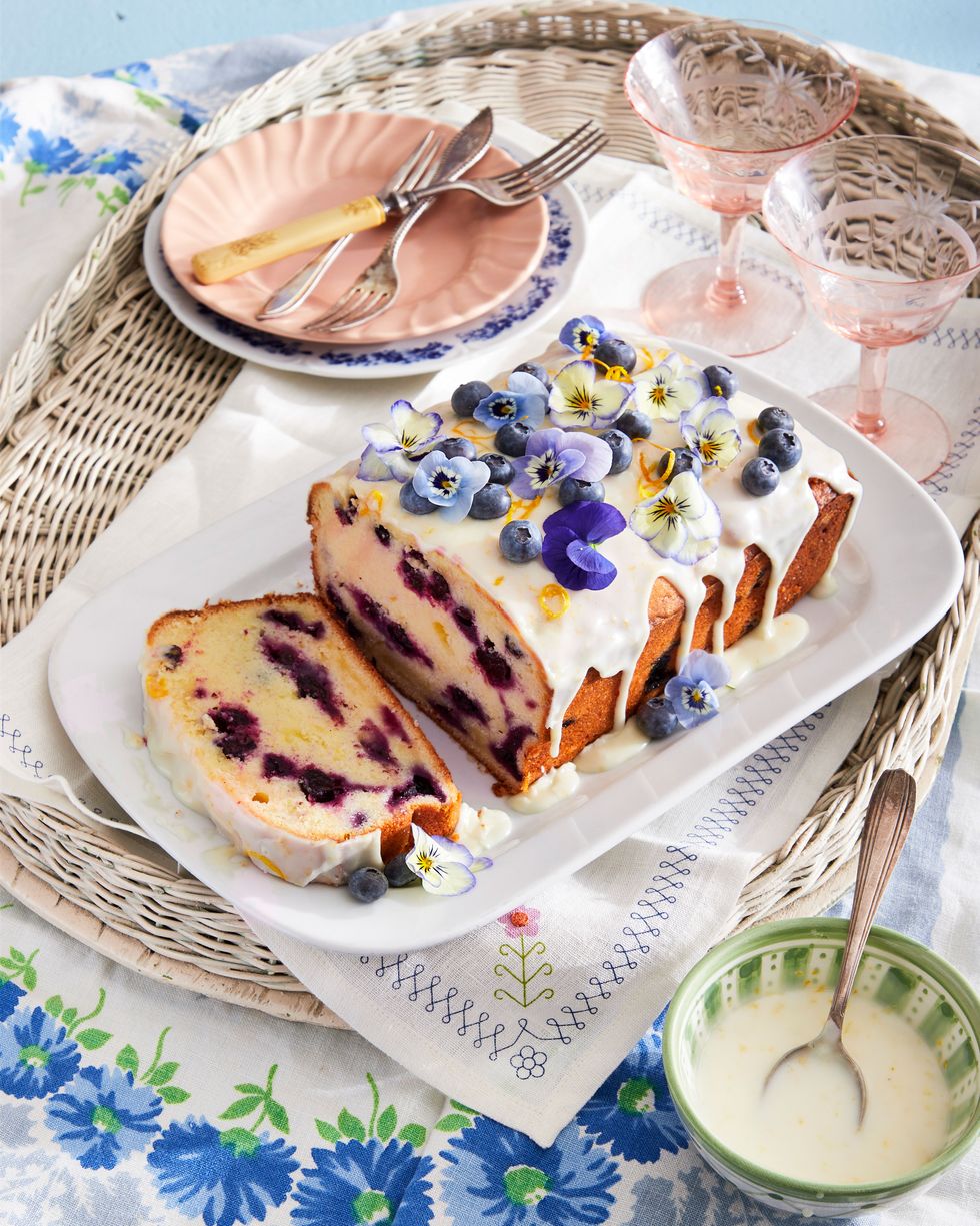blueberry lemon loaf cake on a white plate with lemon icing and decorated with fresh blueberries and pansies