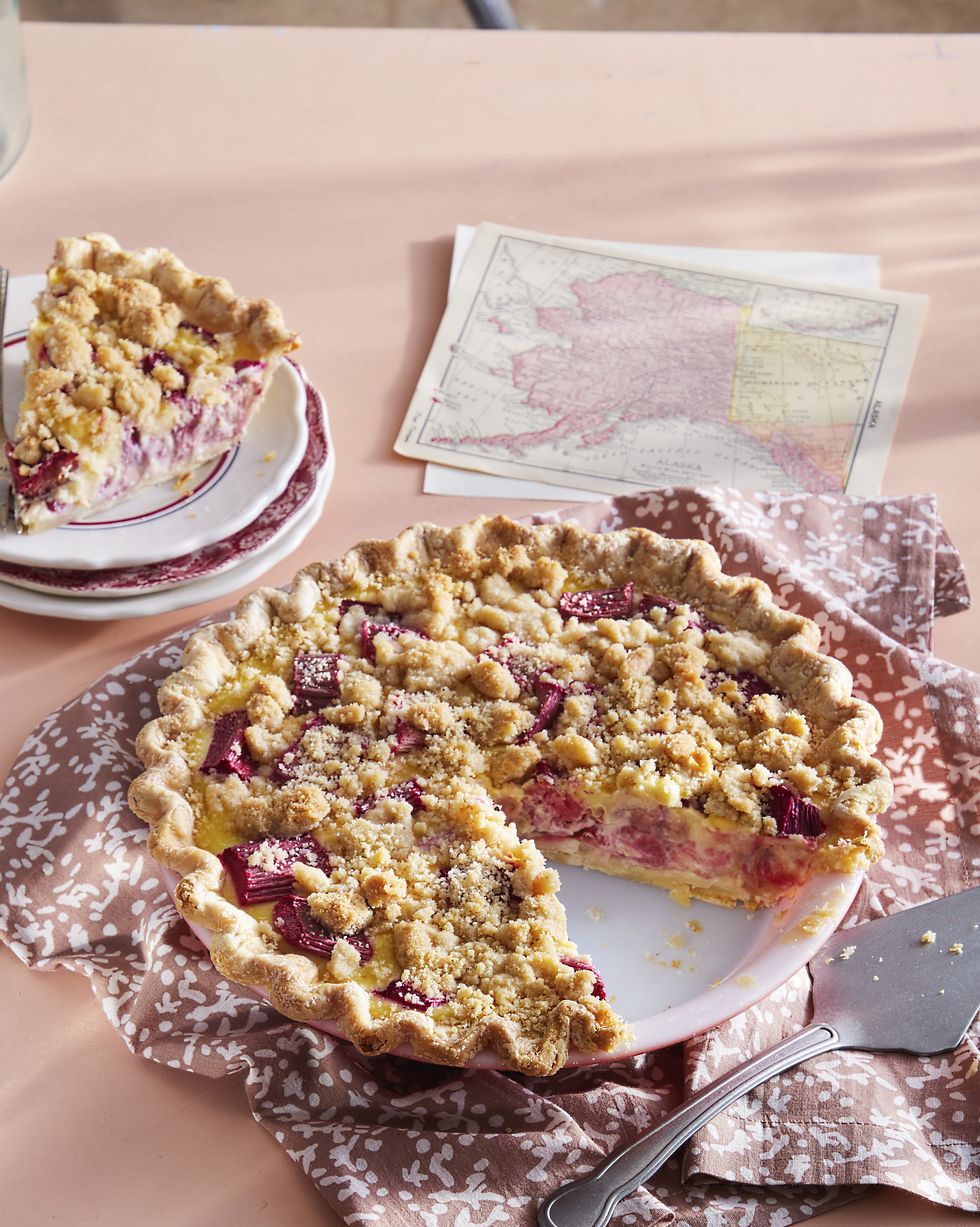 rhubarb custard pie with crumble topping in a white pie plate and a slice removed on a small plate to the side
