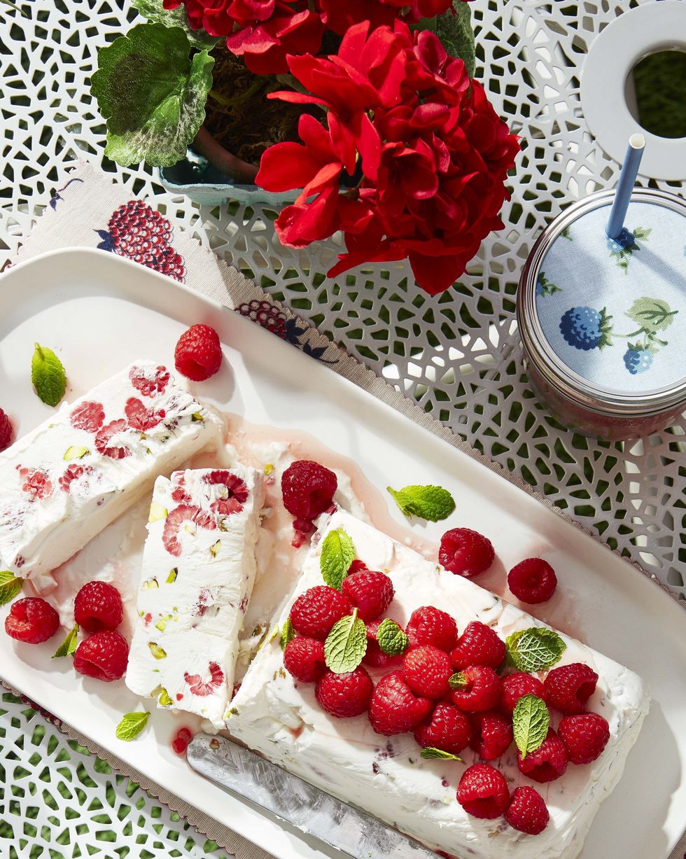 raspberry and pistachio semifreddo on a white serving tray with fresh raspberries and mint leaves on top