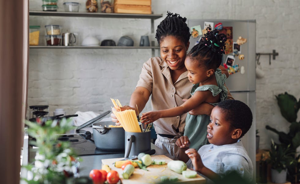 mother daughter and son preparing spaghetti and vegetables for lunch over a cutting board