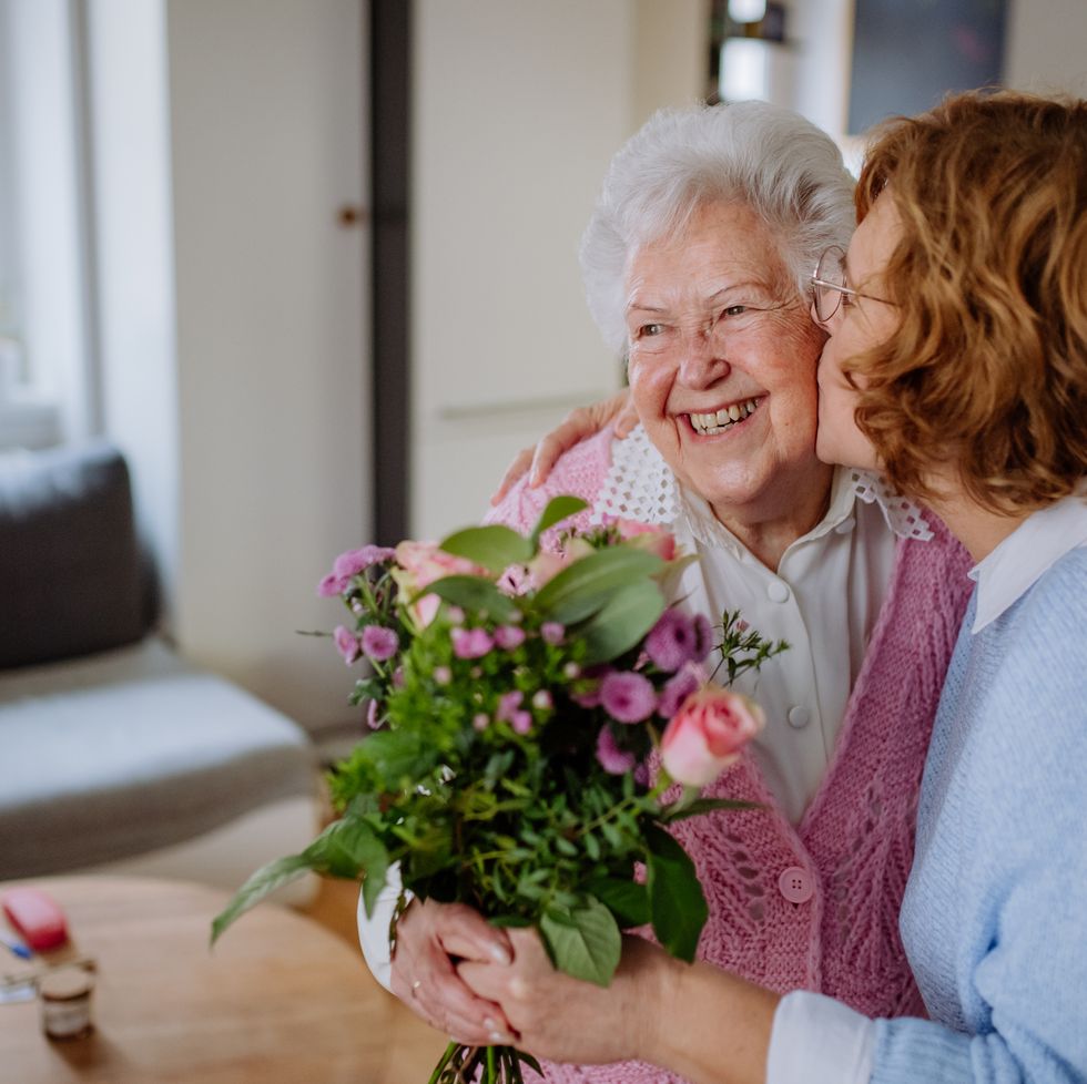 mature woman visiting her older senior mother at home bringing her bouquet