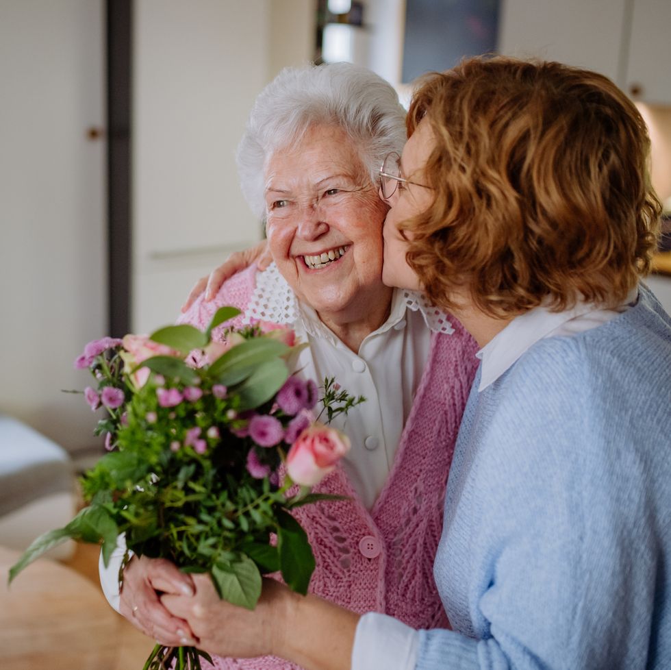 mature woman visiting her older senior mother at home bringing her bouquet