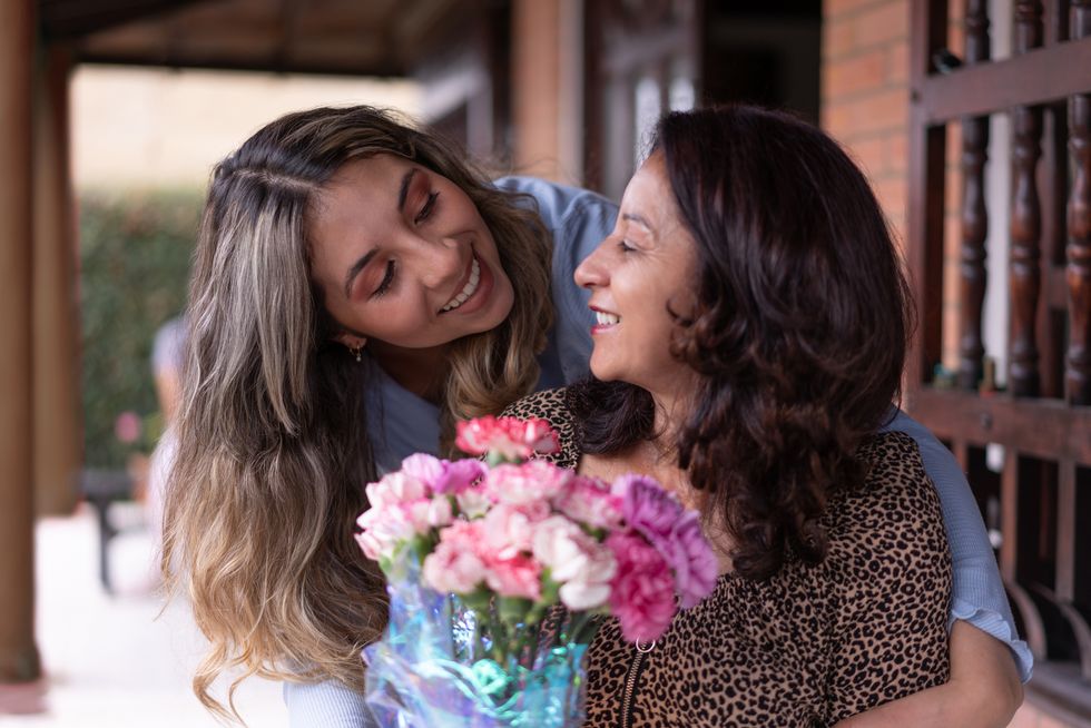 loving daughter hugging mom from behind surprising her with flowers for motherâs day celebration concepts