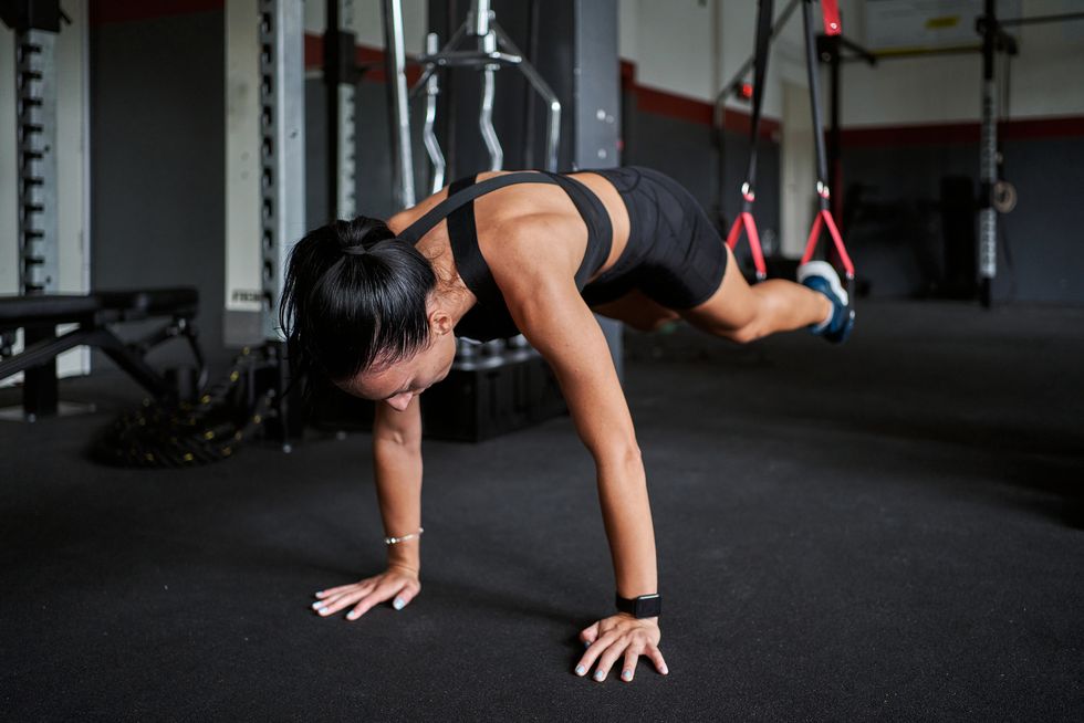 motivated young sportswoman in a plank position while doing a suspension training at the gym