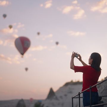 a young female tourist is taking photos of hot air balloons from the rooftop of the hotel where she is staying during her travel
