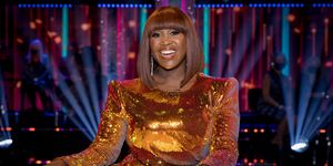 strictly come dancing judge motsi mabuse wearing an orange sequinned dress, sitting behind her desk