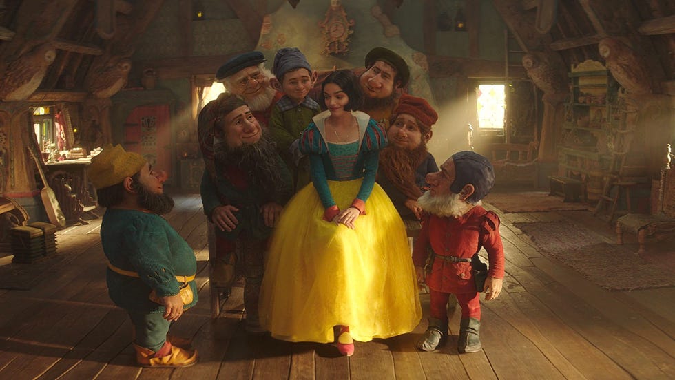 snow white sits peacefully on a chair surrounded by dwarves in a scene from disney's snow white, a good housekeeping pick for best kids' movies 2025