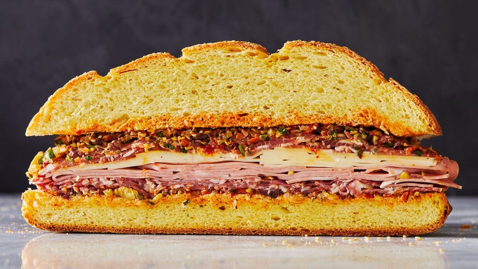 a layered muffuletta sandwich with meat, cheese, and olive salad