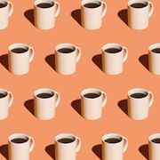 Mugs of black coffee in rows against peach background