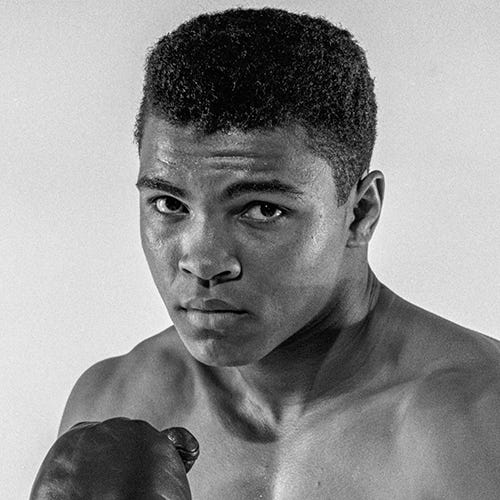 black and white photo of muhammad ali, facing the camera with boxing gloves on