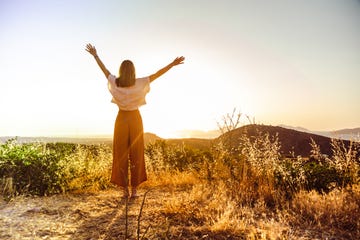 mujer en el campo levantando los brazos mientras ve un amanecer