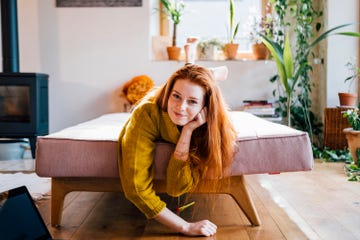 una mujer joven con el pelo largo pelirrojo tumbada en un sofa rosa
