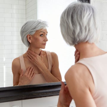 Una mujer con el pelo con canas se mira al espejo una mujer se mira al espejo con sus primeras arrugas