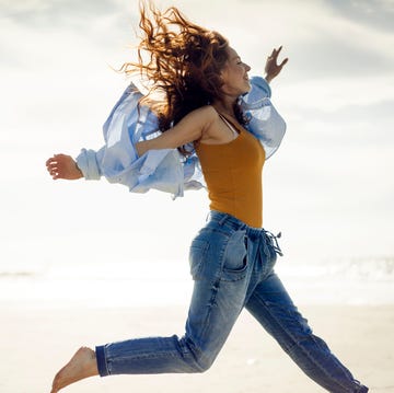 Una mujer feliz salta en la playa una chica con vaqueros, camisa y el pelo suelto salta en una playa