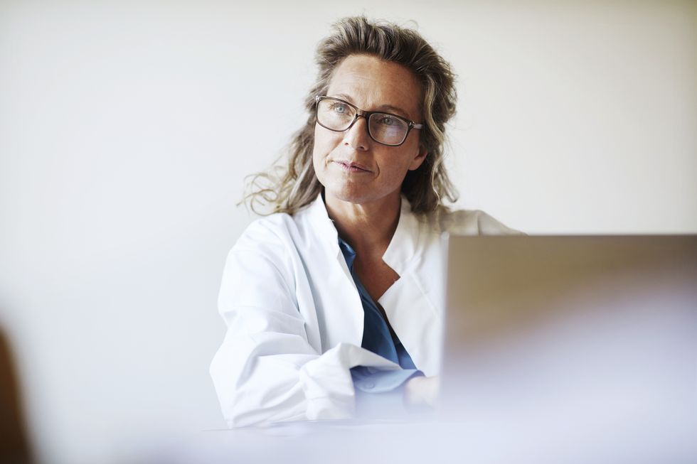 una doctora con gafas y el pelo recogido porta una bata y utiliza un ordenador