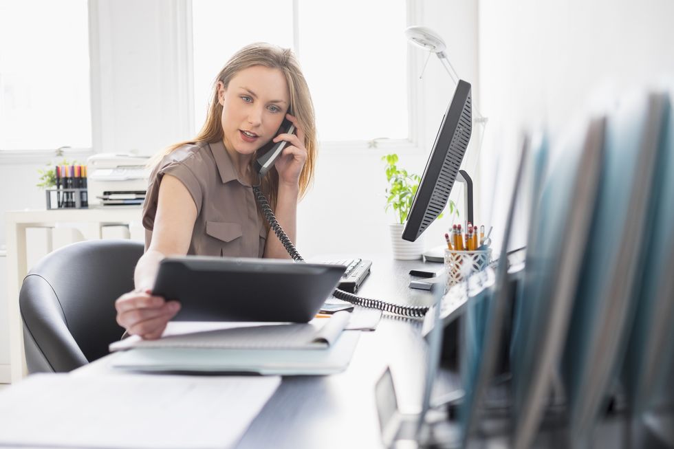 una mujer joven atiende al teléfono en una oficina mientras consulta un documento