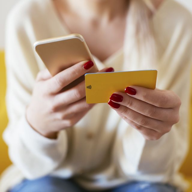 una mujer sostiene una tarjeta de crédito mientras hace una compra online con el móvil en una casa