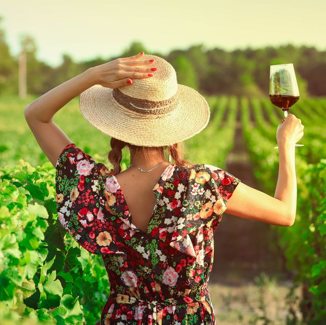 mujer alzando una copa de vino en un campo de viñas