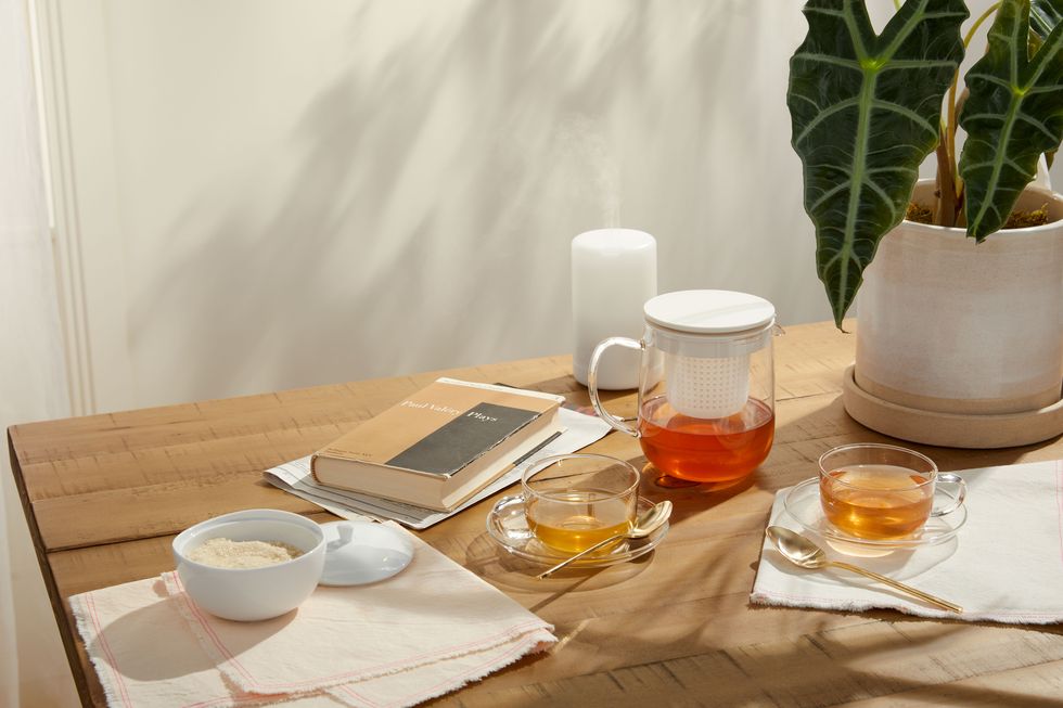 clear tea set next to book, plant, diffuser, and jar on wood table