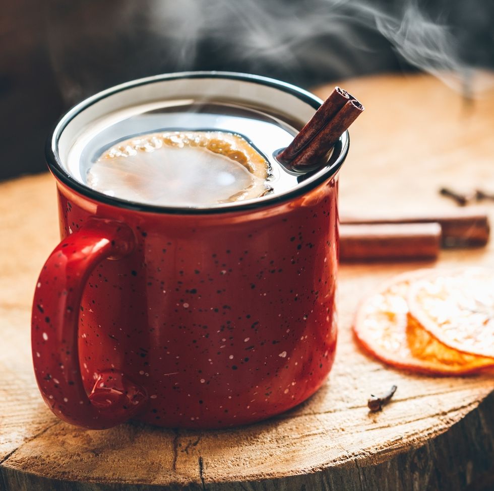 mulled wine in a red ceramic mug over rustic wooden boards suppounded spices