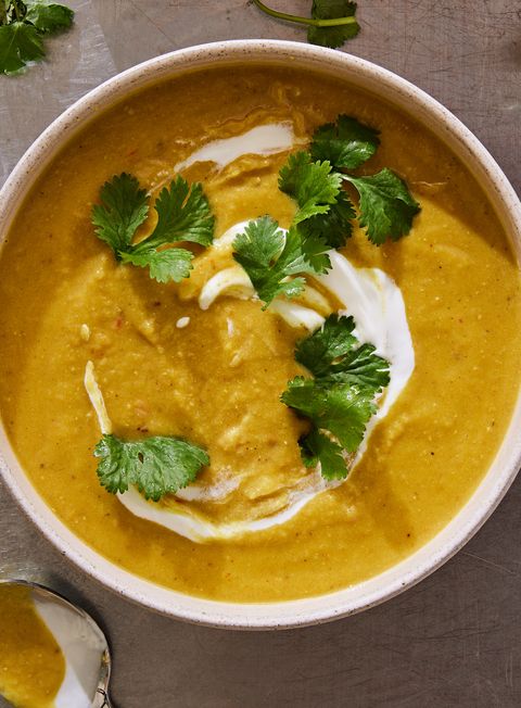 golden yellow mulligatawny soup garnished with yogurt and cilantro in a white bowl