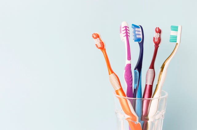 multi colored toothbrushes in a glass cup, blue background