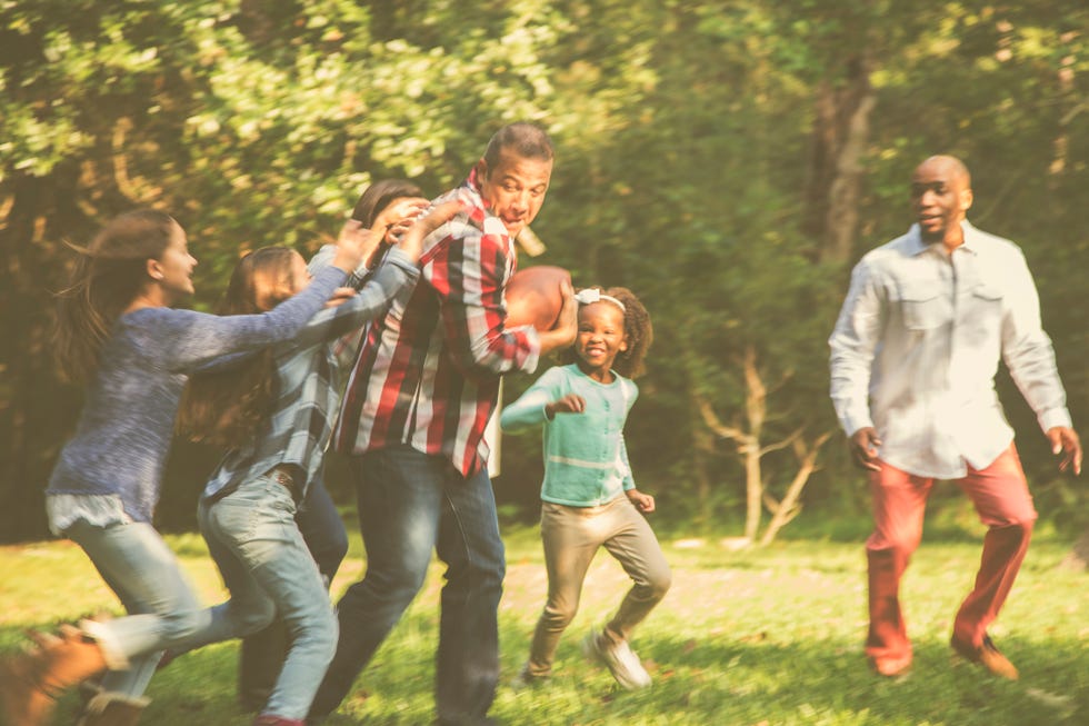 multi ethnic family playing football in backyard at thanksgiving