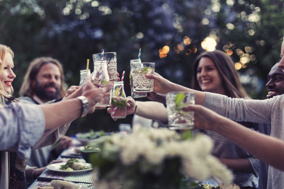 multi ethnic friends toasting mojito glasses at dinner table in yard