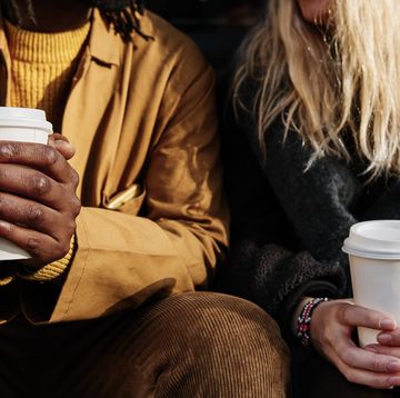 multicultural unrecognizable friends holding a paper cup of coffee while sitting together focus on the hands