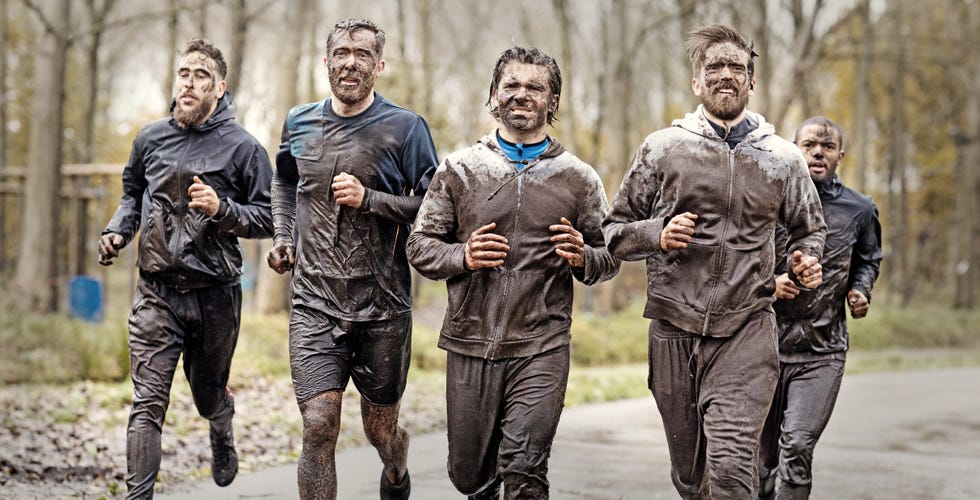 multiethnic mud run team of men running during obstacle course