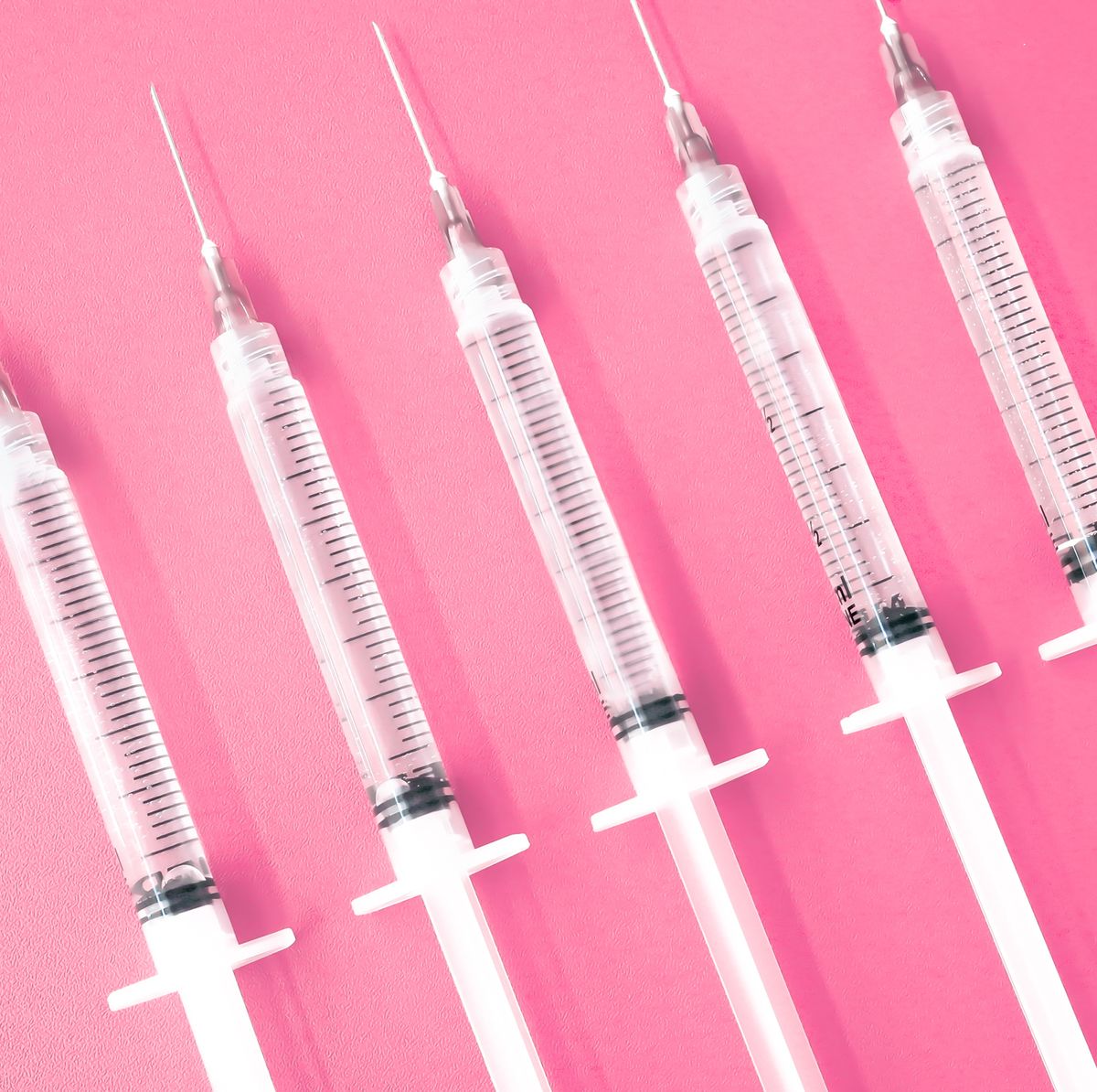 multiple syringes with needles on pink background