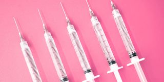 multiple syringes with needles on pink background