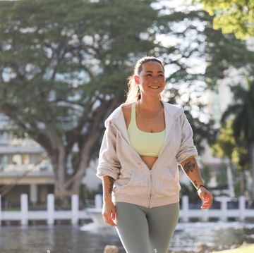 a multiracial millennial woman walks along a river in a tropical climate city while wearing athletic clothing