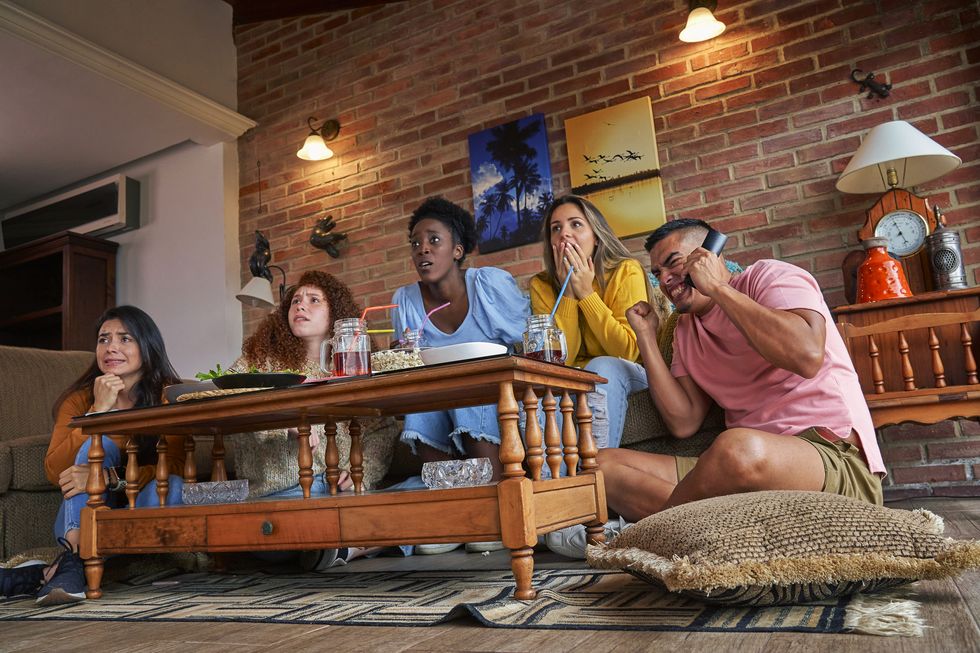 multiracial small group of young people having fun watching a sport game on tv during home party