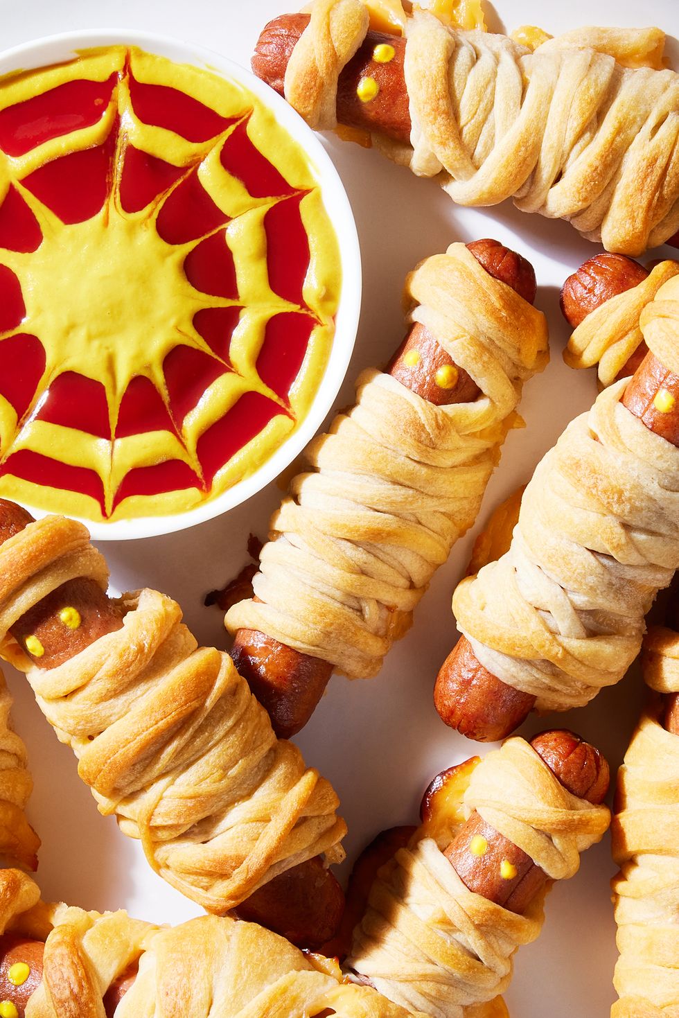 hot dogs with mustard eyes wrapped in crescent dough with cheese and served a mustard and ketchup dip