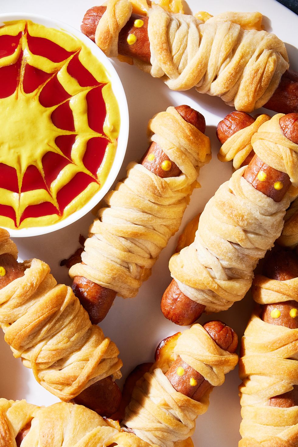 hot dogs with mustard eyes wrapped in crescent dough with cheese and served a mustard and ketchup dip
