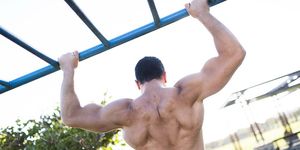muscular back of young man doing pull ups in public park