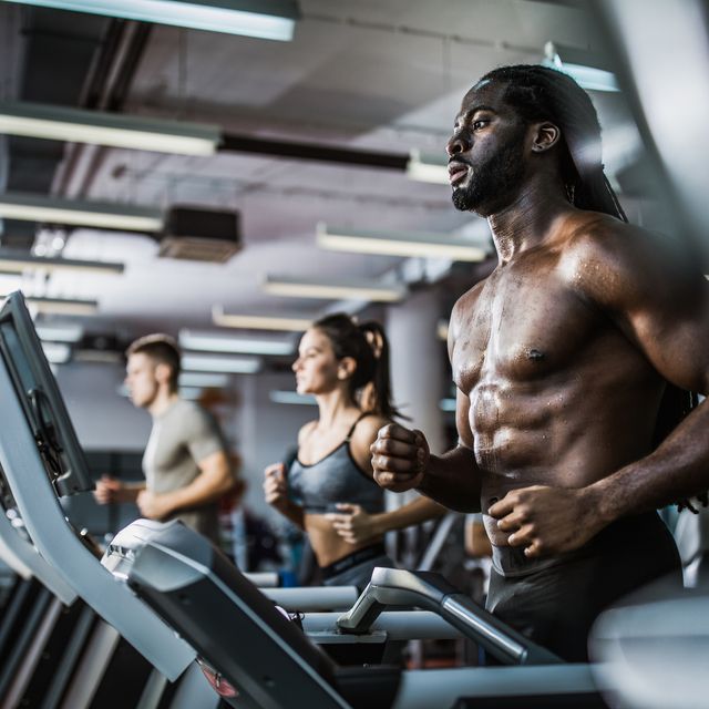 Muscular build black man warming up on treadmill in a health club.