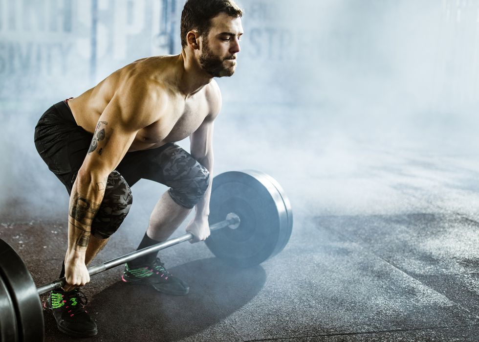 muscular build man exercising deadlift with barbell in a health club