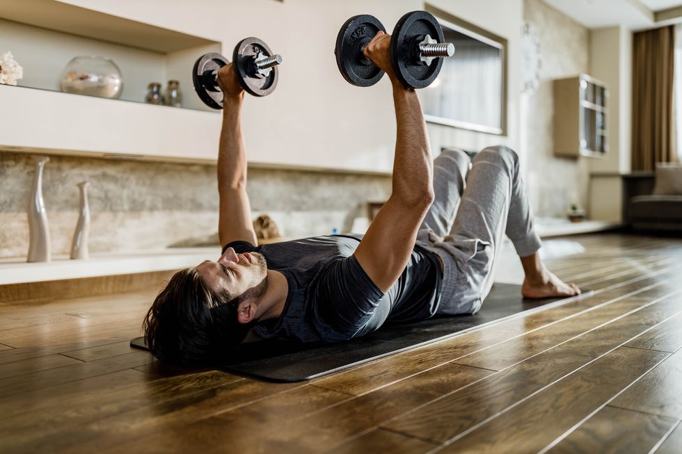 muscular build man exercising strength with weights on a floor