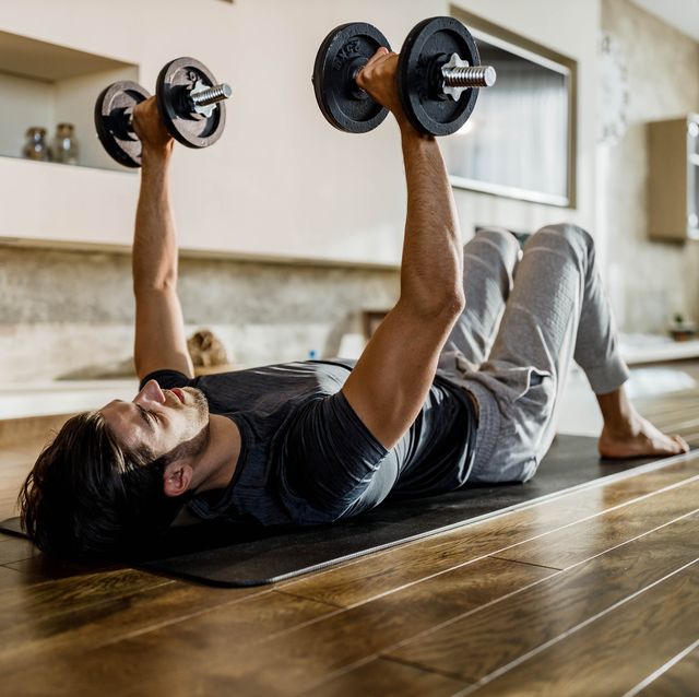 muscular build man exercising strength with weights on a floor