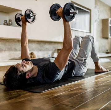 muscular build man exercising strength with weights on a floor