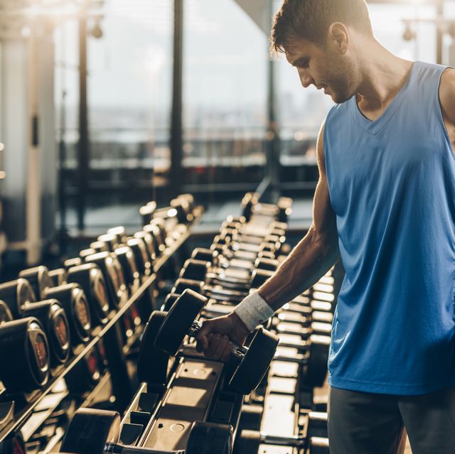 muscular build sportsman taking weights from a rack in a gym.